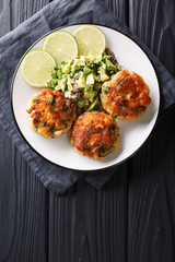 Delicious healthy salmon fritters with avocado salsa and lime closeup on a plate. Vertical top view