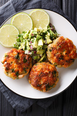Freshly made salmon burgers with avocado salsa and lime close-up on a plate. Vertical top view