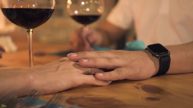 Male hand touching female hand while romantic date in evening restaurant. Woman touching hand girlfriend on table at evening dinner in elegant cafe. Romantic people relationships.