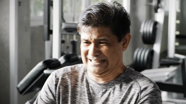 Senior asian man trying to use a low row training machine in gym, trying very hard. Senior Fitness lifestyle.
