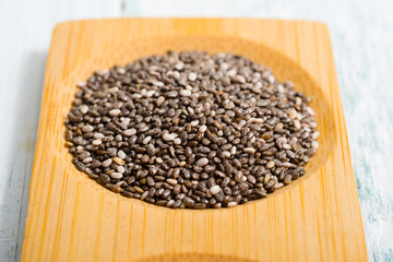 pile of uncooked chia seeds on bamboo, white wooden table