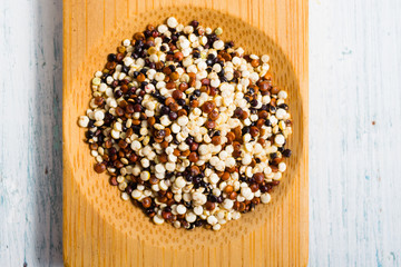 pile of quinoa seeds on bamboo, white wooden table