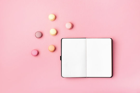 Notebook And Colorful Macaron On Pastel Pink Desk Top View. Fashion Flat Lay. Sweet Macaroons.