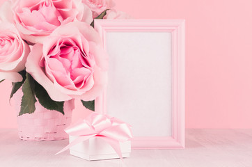 Romance festive interior - delicate pastel pink flowers, blank frame and gift box with gentle ribbon and bow on white wooden table, closeup.