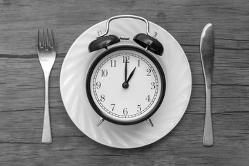 Fototapeta na wymiar Alarm clock with fork and knife on the table. Time to eat, Breakfast, Lunch time and dinner concept. Black and White Concept