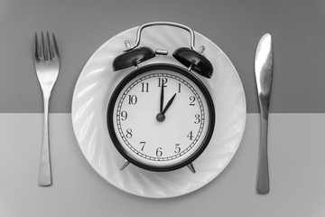 Alarm clock with fork and knife on the table. Time to eat, Breakfast, Lunch time and dinner concept. Black and White Concept