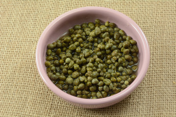 Close up of capers cooking ingredient in pink condiment bowl on burlap