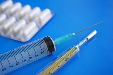 Medical preparation.A syringe and a thermometer on a blue background.