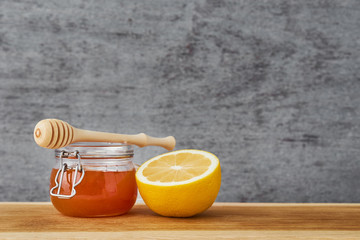 Honey in glass jar and lemon on a wooden table close up with copy space