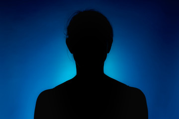 Cleanly defined silhouette of a person against a blue background with a spotlight and bright area right behind it