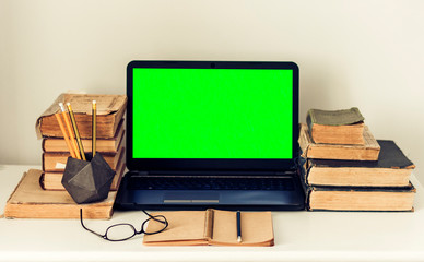 Green screen laptop, stack of old books, notebook and pencils on white table, education office concept background.