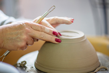 Womans hands making pot from clay on pottery wheel