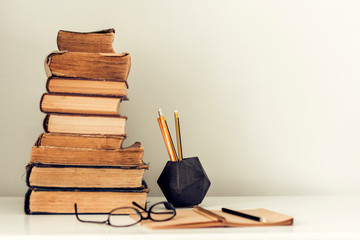 Stack of old books, textbook, glasses and pencils in office background for education retro concept.