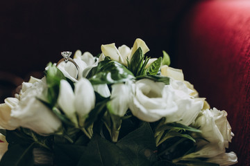 wedding ring of the bride lies on a bouquet of white flowers and greenery