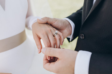 the bride in a white dress and the groom in a suit put the wedding ring on each other