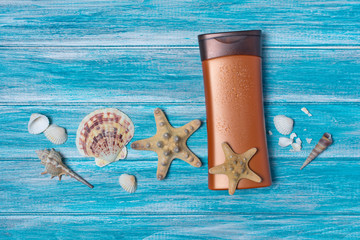 Bronze bottle with sunscreen and seashells on blue background as concept of vacation time
