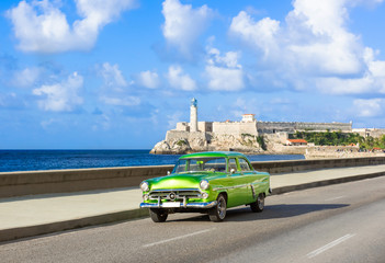 Amerikanischer grüner Cabriolet Oldtimer auf dem berühmten Malecon und im Hintergrund die Festung Castillo de los Tres Reyes del Morro in Havanna Kuba - Serie Kuba Reportage - obrazy, fototapety, plakaty