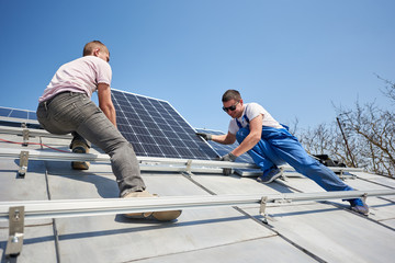 Male workers installing stand-alone solar photovoltaic panel system. Two electricians mounting blue...