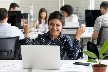 Excited woman sitting at desk looking at computer screen