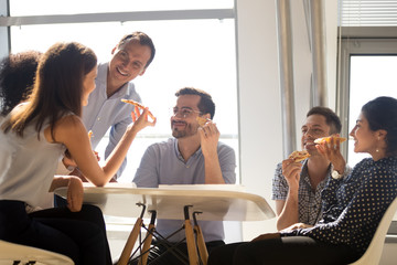 Colleagues eating pizza during lunch sitting together in office 