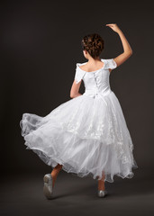Fototapeta premium little girl is dancing in a white ball gown, dark background
