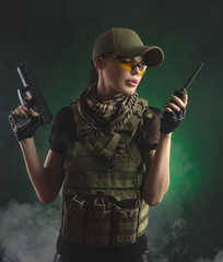 the girl in military special clothes posing with a gun in his hands on a dark background in the haze