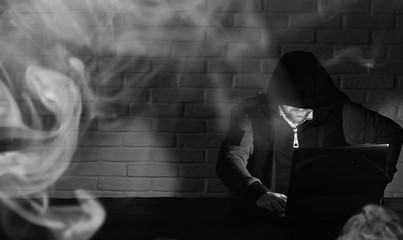 Fototapeta na wymiar Hacker in black mask and hood at the table