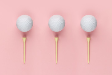 Three golf ball and wooden tee on pink background closeup