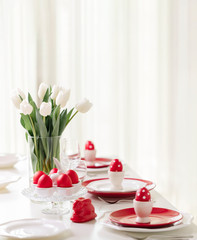 Happy easter. Decor and table setting of the Easter table is a vase with white tulips and dishes of red and white color. Easter colored eggs with white polka dots.