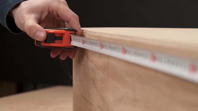 A close-up of man's hand measuring with a flexible ruler the length of wooden workpiece