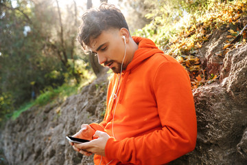 Sports fitness man runner outdoors in park listening music with earphones using mobile phone.