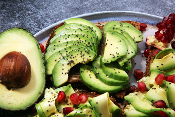 sliced avocado and ripe pomegranates on toast bread with spices and avocado.