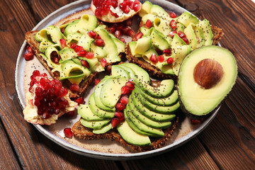 sliced avocado and ripe pomegranates on toast bread with spices and avocado.