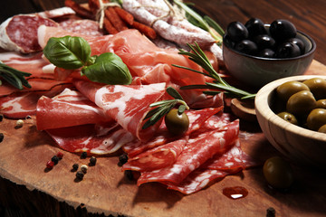 Marble cutting board with prosciutto, bacon, salami and sausages on wooden background. Meat platter