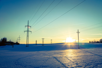 Electrical tower on a snowy field. Sun goes down, orange colors, evening scenery