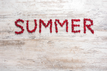 word "Summer" made of raspberry berries on a textured light wooden background. Flat top view, place for text. Flat lay, Copy space.