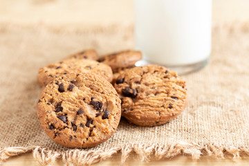 A stack of chocolate chip cookies and bottles of milk on sackcloth on wood table.