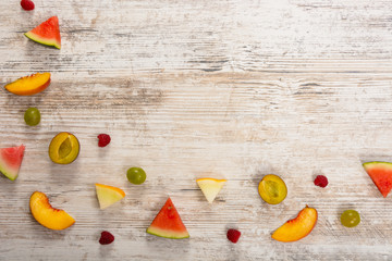 Pieces of fruit, apple, peach, melon, watermelon, grapes, plum, raspberry, lie on a textured light wooden background. Flat top view, place for text. Flat Lay, Copy Space. Summer background.