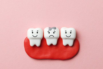 Healthy white teeth are smiling and tooth with caries is sad on pink background.