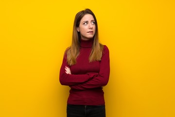 Obraz premium Woman with turtleneck over yellow wall with confuse face expression while bites lip