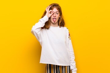 Young redhead woman over yellow wall makes funny and crazy face emotion