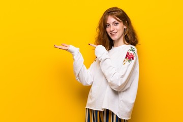 Young redhead woman over yellow wall holding copyspace imaginary on the palm to insert an ad