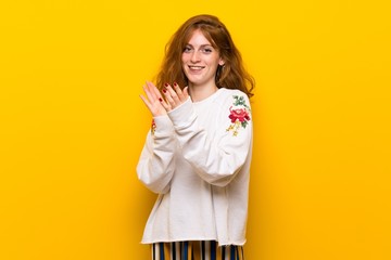 Fototapeta premium Young redhead woman over yellow wall applauding after presentation in a conference