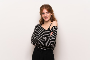 Young redhead woman over white wall keeping the arms crossed in frontal position