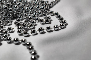 Beautiful round silver beads and beads on white fabric background. Glossy shiny grey surface....
