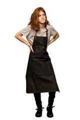A full-length shot of a Young redhead woman with apron suffering from backache for having made an effort over isolated white background