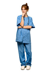 A full-length shot of a Young redhead nurse looking to the side with the hand on the chin over isolated white background