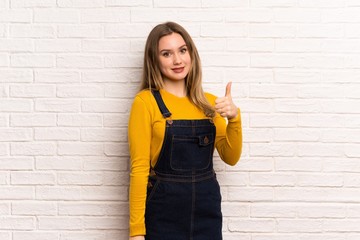 Teenager girl over white brick wall giving a thumbs up gesture and smiling