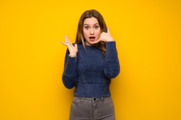 Teenager girl over yellow wall making phone gesture and doubting