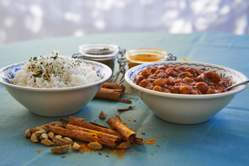 Close up picture of indian dish served in garden of indian restaurant made from spicy hot chickpea curry with basmati rice in bowls, white napkin and jars with curry powder, spices and cinnamon sticks